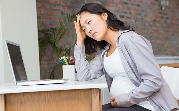 woman looking at a computer while uncomfortable and pregnant